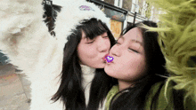 two girls are kissing in front of a tea shop