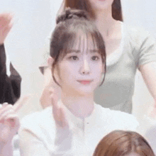 a woman in a white shirt is sitting in front of a group of people and making a peace sign .