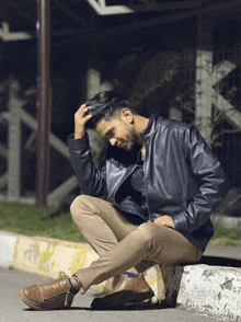 a man in a leather jacket is sitting on a curb
