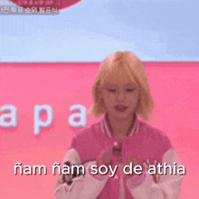 a girl in a pink jacket says n'am n'am soy de athia in front of a pink background