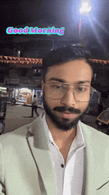 a man with glasses and a beard is standing in front of a good morning sign