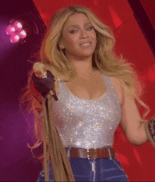 a woman singing into a microphone wearing a silver tank top