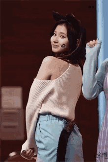 a woman wearing a white sweater and blue pants has a cat tail on her back .