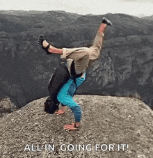 a man is doing a handstand on top of a rocky mountain .