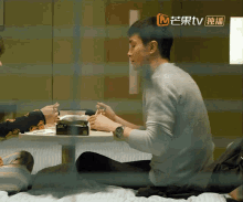 a man sits at a table with a box of tissues in front of him with a tv logo in the corner