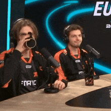 two men are sitting at a table with microphones and one of them is wearing a shirt that says fanaic
