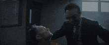 a man in a suit is standing in a dark room with smoke coming out of a window .