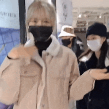 a woman wearing a mask and a jacket is standing next to another woman wearing a mask and a hat .