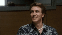 a man wearing a pearl necklace and a hawaiian shirt smiles
