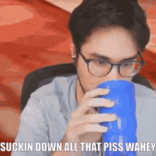 a man with glasses is drinking from a blue cup with the words suckin down all that piss wahey
