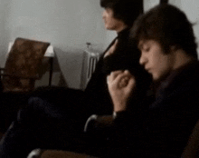 a blurry picture of two men sitting in chairs one smoking a cigarette