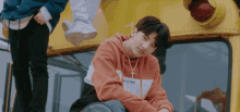 a boy wearing an orange hoodie with a cross on it sits on a yellow bus
