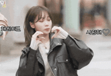 a woman in a black leather jacket making a heart shape with her hands