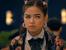 a woman wearing a floral jacket and pink hoop earrings looks angry
