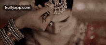 a close up of a woman 's face with a ring on her finger and a necklace on her head .