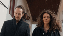 a man and a woman are standing next to each other in a hallway . the woman is wearing a black jacket .