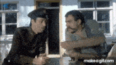 two men are sitting at a table and talking to each other .