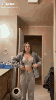 a woman in a crop top and sweatpants is standing in a bathroom ..