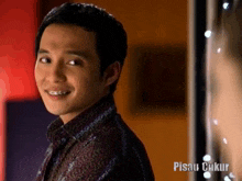 a man with braces on his teeth is smiling in front of a sign that says pisau cukup