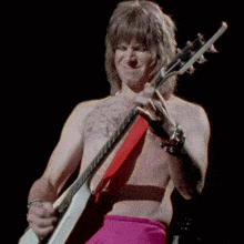 a shirtless man is playing a guitar in a dark room