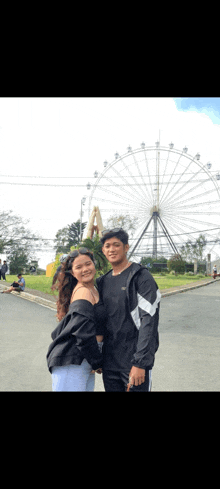 a man and woman are posing for a picture in front of a ferris wheel .