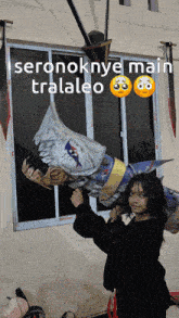 a girl is holding a shark puppet in front of a window that says " seronoknye main traaleo " on it