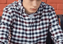 a young man wearing a plaid shirt is sitting in front of a laptop computer .
