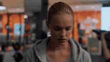 a woman in a gray hoodie is looking down in a gym