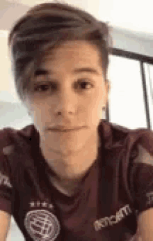 a young man wearing a maroon shirt is making a face .