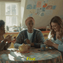 three women are sitting at a table and one of them is saying " five "