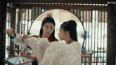 two women are standing next to each other in a room with a fence in the background .