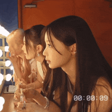three girls are applying makeup in front of a mirror and the time reads 00 : 00 : 09