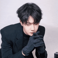 a young man wearing black gloves and a black suit