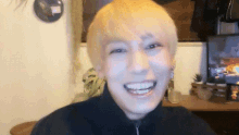 a man with short blonde hair is smiling in front of a television
