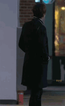 a man in a black coat is standing in front of a brick building