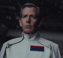 a man in a white uniform has a red blue and white badge on his chest