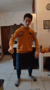 a young boy is dancing in a kitchen wearing a yellow sweatshirt and gray socks .