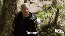 a man in a black jacket is standing in the woods and says tommy on the screen