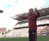 a man in a red kappa jacket is standing on a soccer field