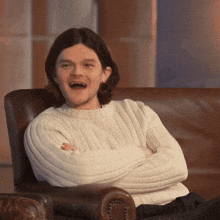 a man wearing a white sweater is sitting on a couch with his arms crossed