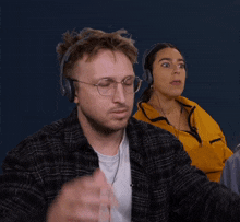 a man wearing glasses and headphones looks surprised while a woman wearing a yellow jacket looks on