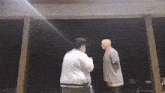 two men are standing next to each other in front of a black wall
