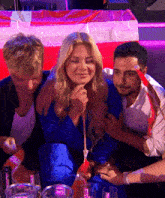 a woman in a blue dress sits between two men in front of a red white and blue flag