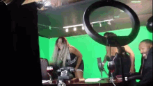 a woman is standing in front of a green screen while a man sits behind her .