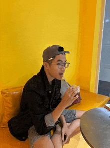 a young man wearing glasses and a hat drinking through a straw