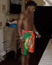 a shirtless man wearing a pair of shorts with a portuguese flag on them is standing on a table .