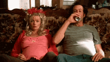 a man and a pregnant woman are sitting on a couch . the man is drinking a can of beer .