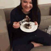 a woman is sitting on a couch eating a plate of food .