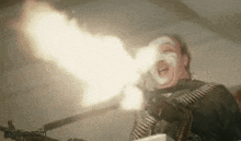 a man with white paint on his face is holding a gun with a lot of fire coming out of it .