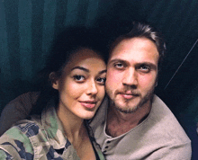 a man and a woman are posing for a picture and the woman is wearing a camouflage jacket